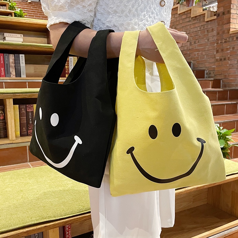 2022 new hand-held smiley face canvas bag female ins style small fresh black yellow wrist Dongdamen shopping bag